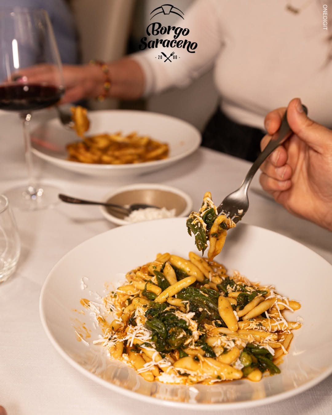Cavatelli con verdure e formaggio grattugiato in piatto bianco, sullo sfondo vino rosso e altra pasta, Borgo Saraceno