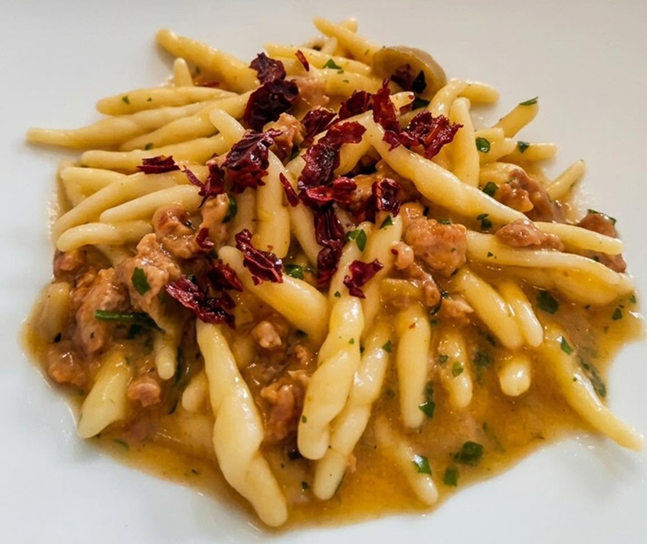 Pasta fresca attorcigliata con salsiccia sbriciolata, prezzemolo e peperoni secchi su piatto bianco di Borgo Saraceno